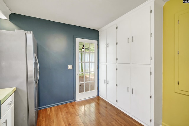 kitchen with light wood-type flooring, white cabinets, stainless steel fridge with ice dispenser, and light countertops