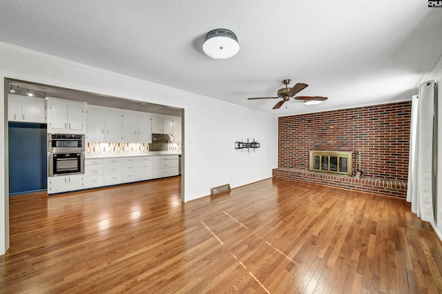 unfurnished living room with brick wall, a fireplace, ornamental molding, ceiling fan, and light wood-style floors