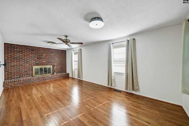 unfurnished living room with visible vents, a textured ceiling, wood-type flooring, brick wall, and a brick fireplace