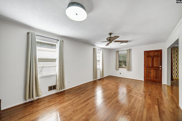 spare room with a ceiling fan, visible vents, ornamental molding, wood-type flooring, and a textured ceiling