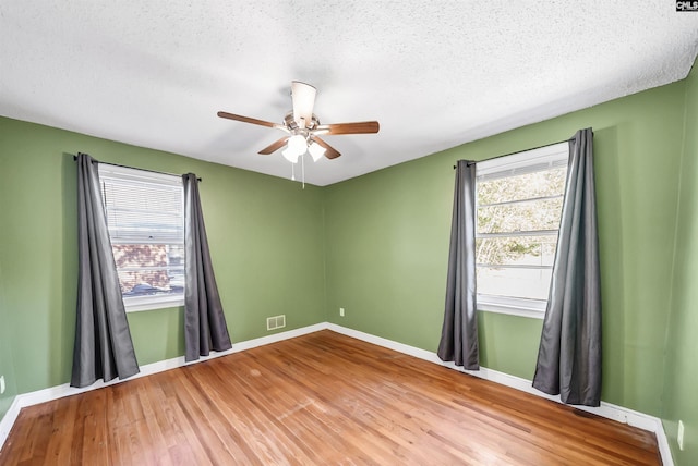 empty room featuring a wealth of natural light, baseboards, a textured ceiling, and wood finished floors