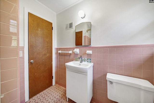 bathroom featuring visible vents, vanity, ornamental molding, wainscoting, and tile walls