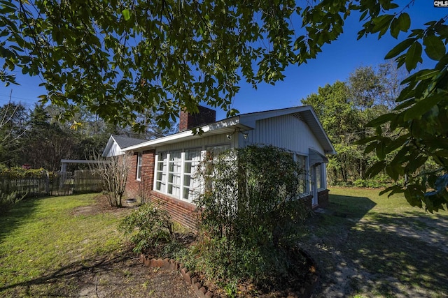 view of side of home featuring brick siding, a chimney, a yard, and fence