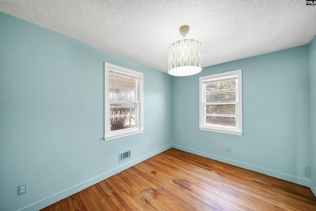 unfurnished room with visible vents, a textured ceiling, baseboards, and wood finished floors