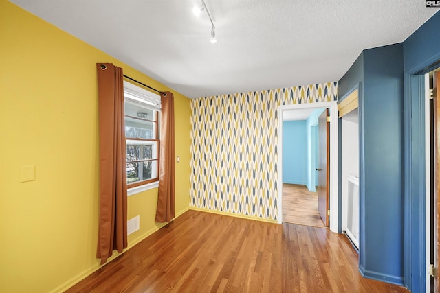 spare room with wood finished floors, visible vents, baseboards, track lighting, and a textured ceiling