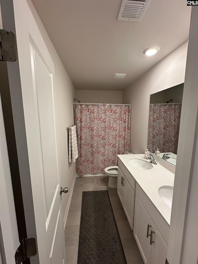 bathroom featuring visible vents, double vanity, a sink, curtained shower, and toilet