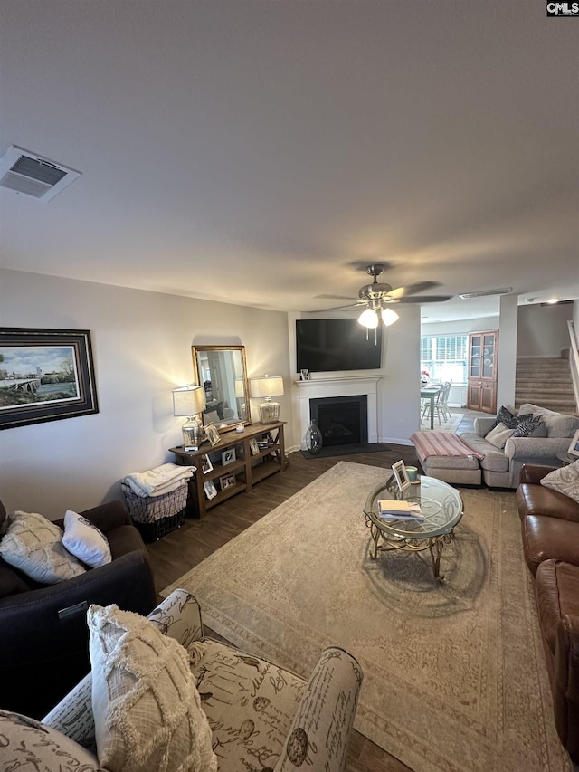 living area with visible vents, a fireplace with flush hearth, a ceiling fan, wood finished floors, and stairs