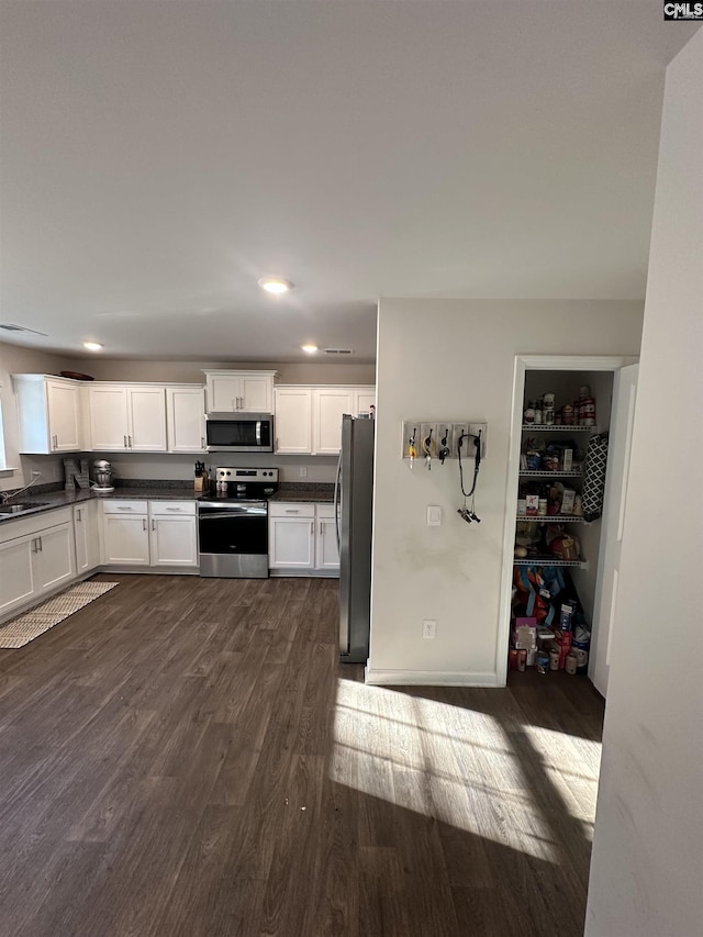 kitchen featuring dark wood-style floors, white cabinets, appliances with stainless steel finishes, and dark countertops