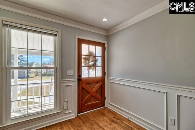 doorway to outside featuring recessed lighting, a wainscoted wall, wood finished floors, and crown molding