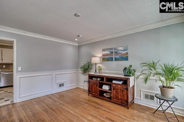 living area featuring a wainscoted wall, visible vents, hardwood / wood-style flooring, a textured ceiling, and crown molding