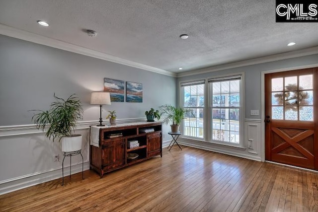 interior space with crown molding, wainscoting, a decorative wall, a textured ceiling, and wood-type flooring