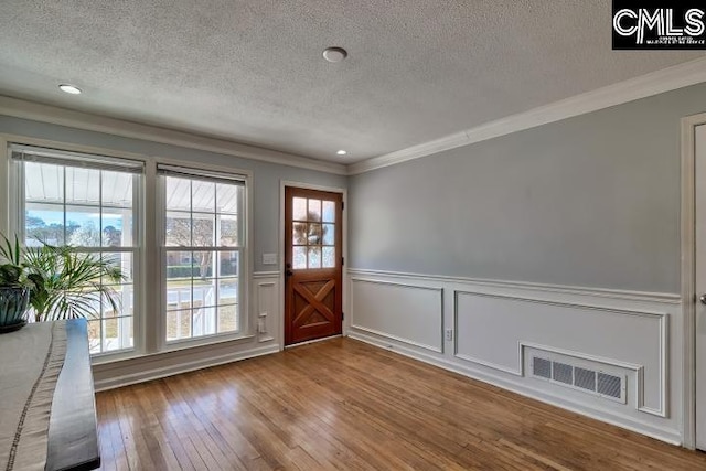 entryway featuring visible vents, wainscoting, wood-type flooring, a textured ceiling, and crown molding