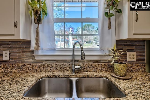 interior details featuring a sink, decorative backsplash, light stone counters, and white cabinets