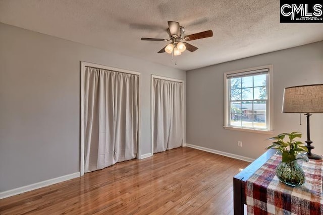 interior space featuring baseboards, a textured ceiling, wood finished floors, and a ceiling fan