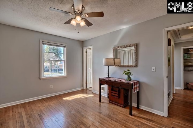 interior space with a ceiling fan, a textured ceiling, hardwood / wood-style floors, baseboards, and attic access