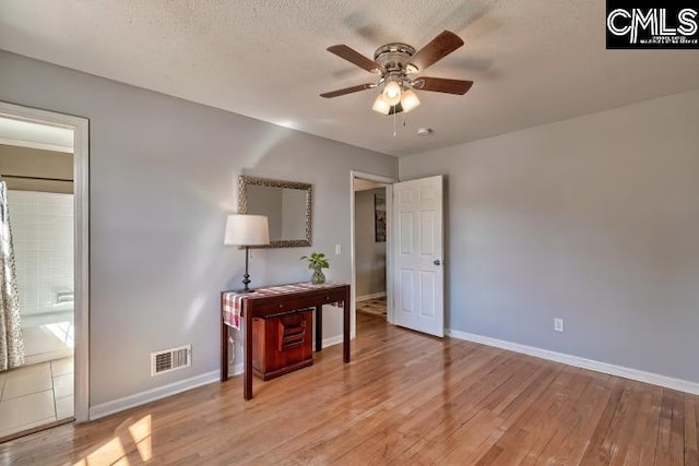 bedroom with baseboards, visible vents, light wood finished floors, and a textured ceiling