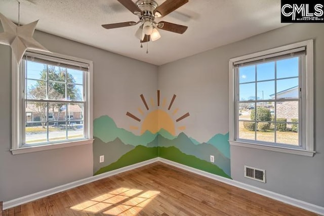 unfurnished room with visible vents, baseboards, wood finished floors, and a ceiling fan