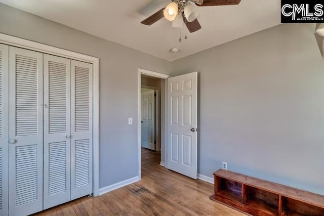 unfurnished bedroom featuring a ceiling fan, wood finished floors, baseboards, and a closet