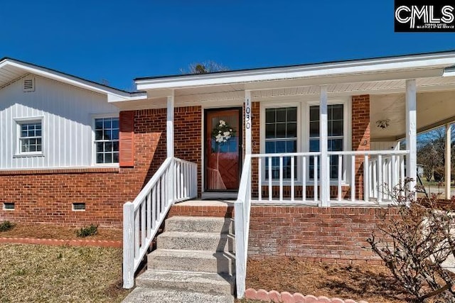 view of exterior entry featuring crawl space, brick siding, and a porch