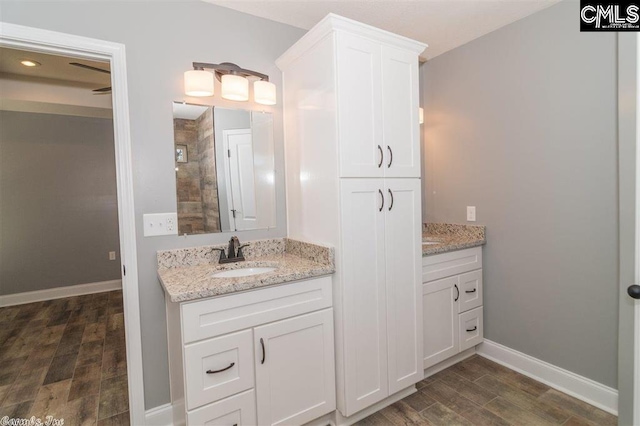 bathroom with tiled shower, baseboards, wood finished floors, and vanity