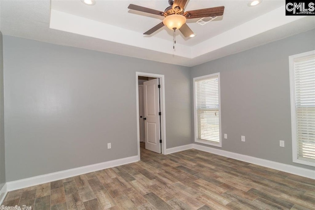 unfurnished room with baseboards, recessed lighting, wood finished floors, a raised ceiling, and a ceiling fan