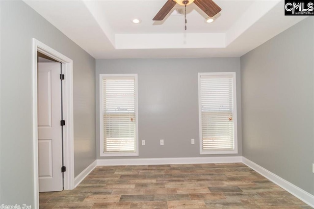 spare room with a raised ceiling, a ceiling fan, wood finished floors, recessed lighting, and baseboards