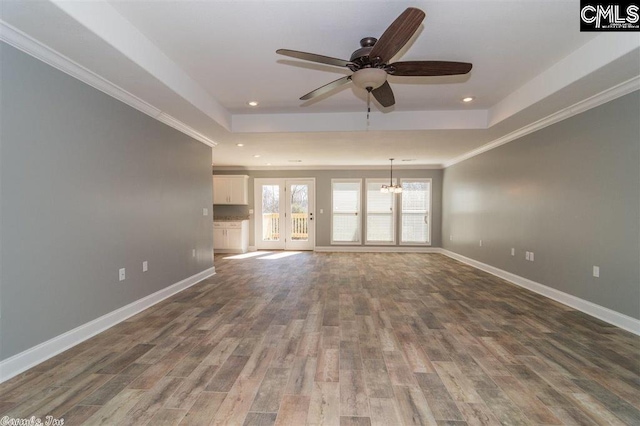 unfurnished living room with a tray ceiling, wood finished floors, and baseboards