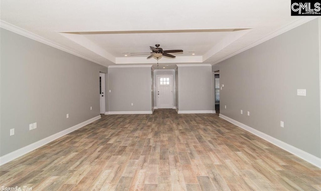 unfurnished living room with a tray ceiling, baseboards, crown molding, and light wood finished floors