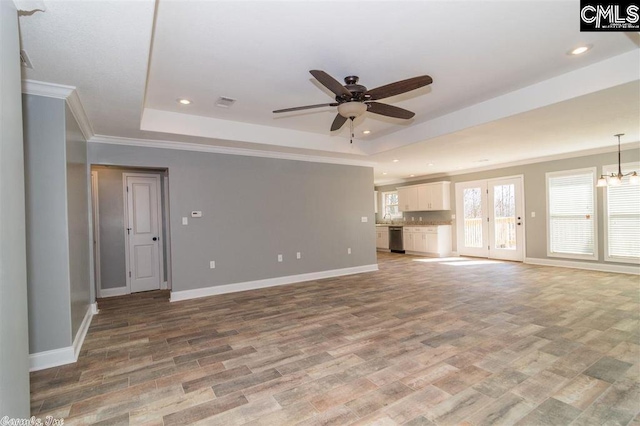 unfurnished living room featuring ceiling fan with notable chandelier, light wood-type flooring, a raised ceiling, and baseboards