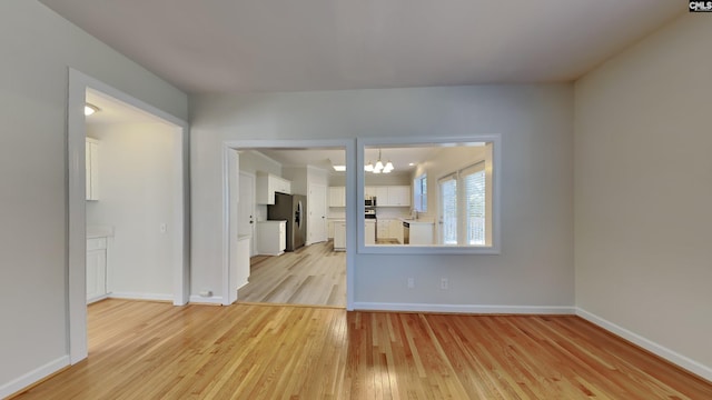 unfurnished room featuring an inviting chandelier, baseboards, light wood finished floors, and a sink