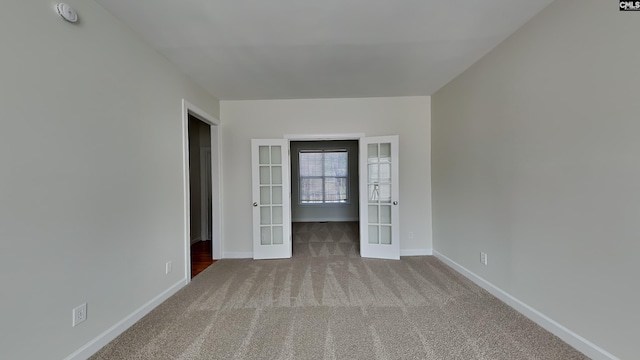 carpeted spare room featuring french doors and baseboards