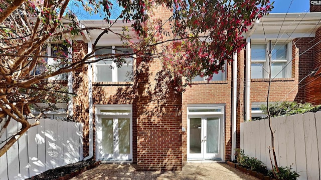 rear view of property featuring brick siding, french doors, and fence