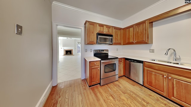 kitchen featuring light wood finished floors, ornamental molding, stainless steel appliances, and a sink