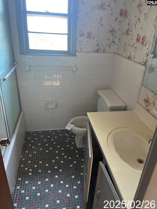 bathroom featuring a wainscoted wall, toilet, shower / bath combination with glass door, wallpapered walls, and vanity