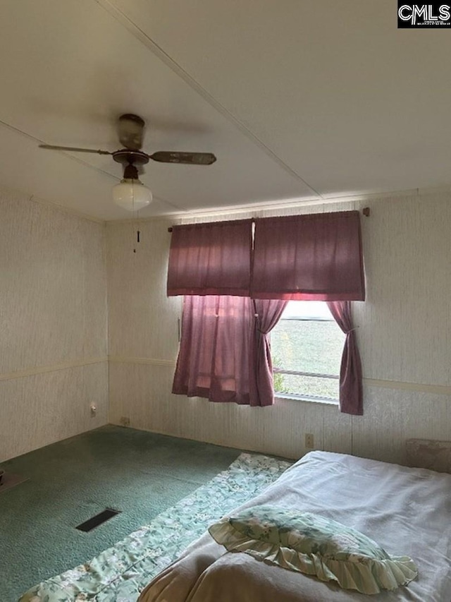 unfurnished bedroom with visible vents, carpet floors, wooden walls, and a ceiling fan