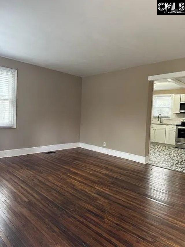 spare room featuring visible vents, a healthy amount of sunlight, dark wood-style flooring, and baseboards