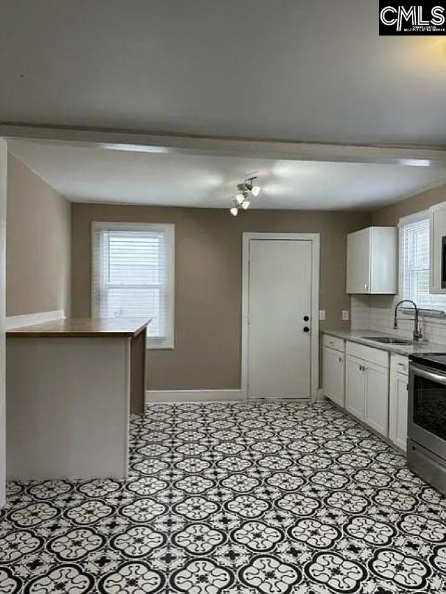 kitchen with baseboards, stainless steel electric range oven, decorative backsplash, white cabinets, and a sink