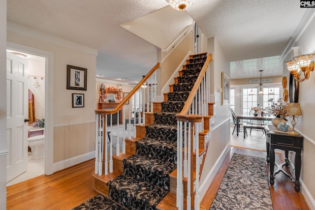 staircase with a textured ceiling, wood finished floors, baseboards, and ornamental molding