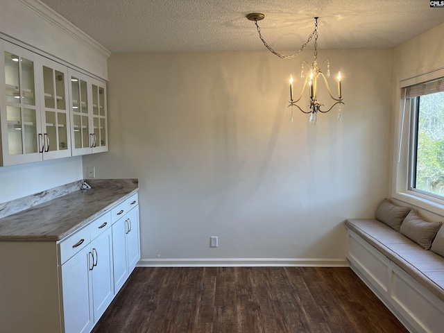 unfurnished dining area featuring dark wood-type flooring, a notable chandelier, baseboards, and a textured ceiling