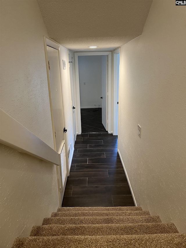 interior space featuring stairway, baseboards, wood finish floors, a textured ceiling, and a textured wall