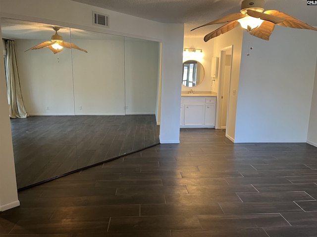 unfurnished living room featuring a ceiling fan, baseboards, visible vents, dark wood finished floors, and a sink