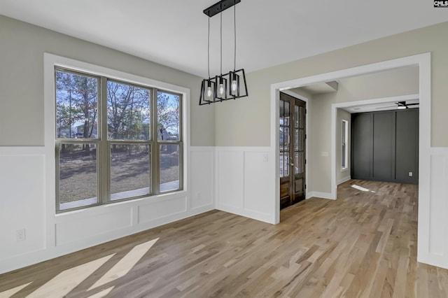 unfurnished dining area with a decorative wall, light wood-type flooring, a chandelier, and wainscoting