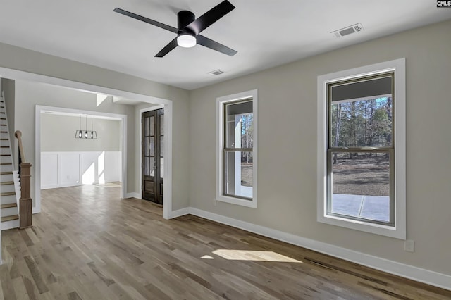 empty room featuring stairs, wood finished floors, visible vents, and baseboards