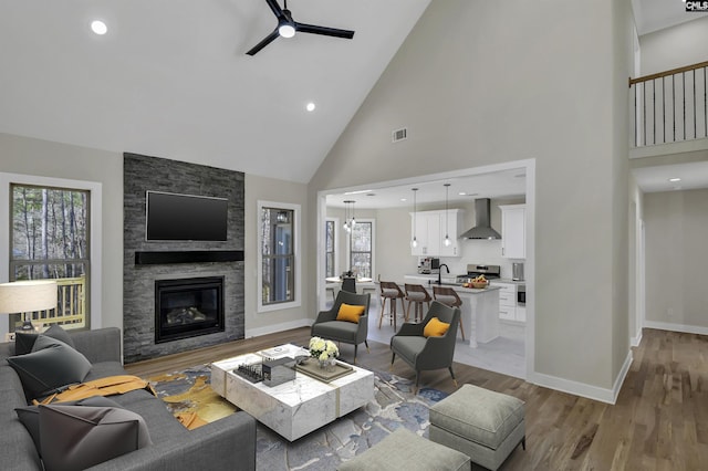 living room with baseboards, visible vents, light wood-style flooring, a fireplace, and ceiling fan