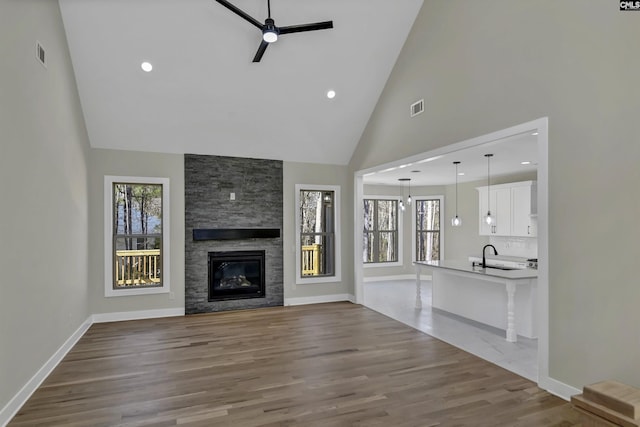 unfurnished living room featuring a stone fireplace, a ceiling fan, visible vents, and a sink