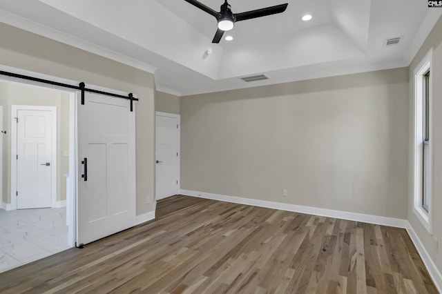 unfurnished bedroom featuring visible vents, baseboards, a barn door, wood finished floors, and a raised ceiling