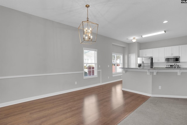 kitchen with baseboards, appliances with stainless steel finishes, pendant lighting, white cabinetry, and a kitchen breakfast bar