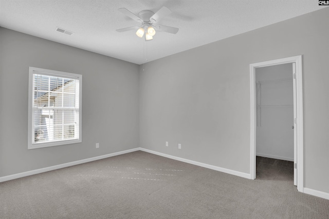 empty room featuring visible vents, a textured ceiling, carpet floors, baseboards, and ceiling fan