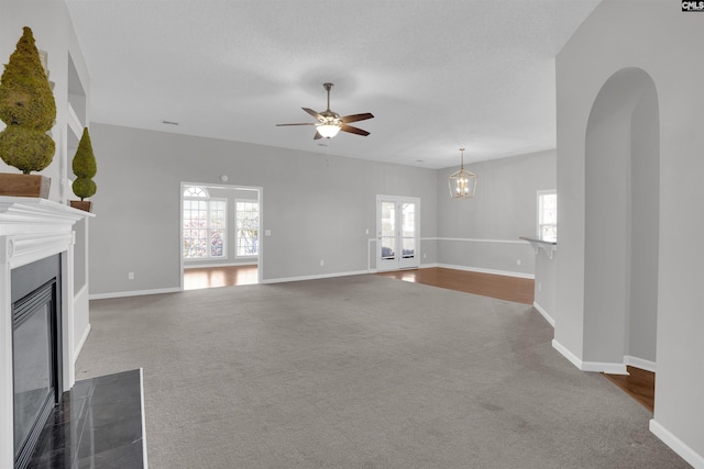 unfurnished living room featuring a fireplace with flush hearth, carpet flooring, ceiling fan with notable chandelier, and baseboards