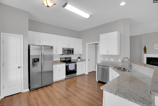 kitchen featuring light wood finished floors, appliances with stainless steel finishes, a peninsula, white cabinetry, and a sink